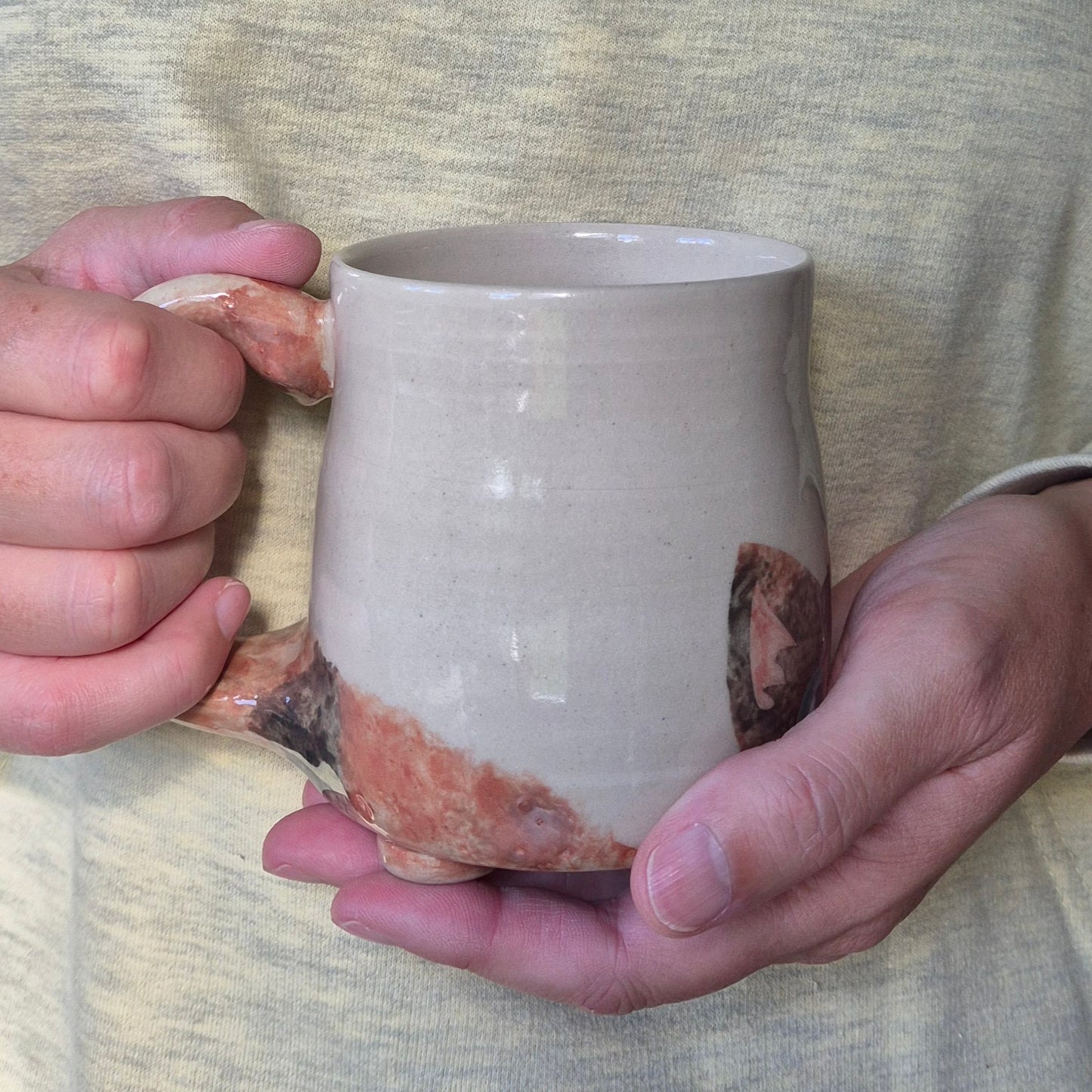 Person holding a ceramic mug with a unique glaze pattern