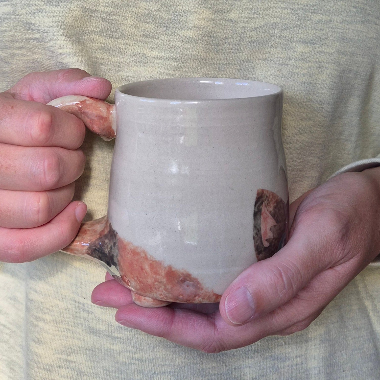 Person holding a ceramic mug with a unique glaze pattern