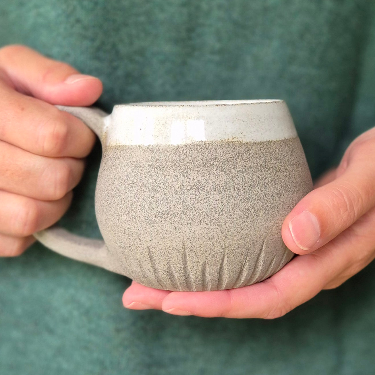 Person holding a textured ceramic mug against a green background