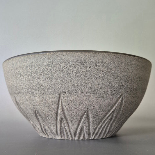 Textured ceramic bowl with carved  patterns on a gray background