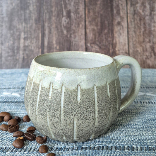Ceramic mug with textured design on a textured surface with coffee beans.