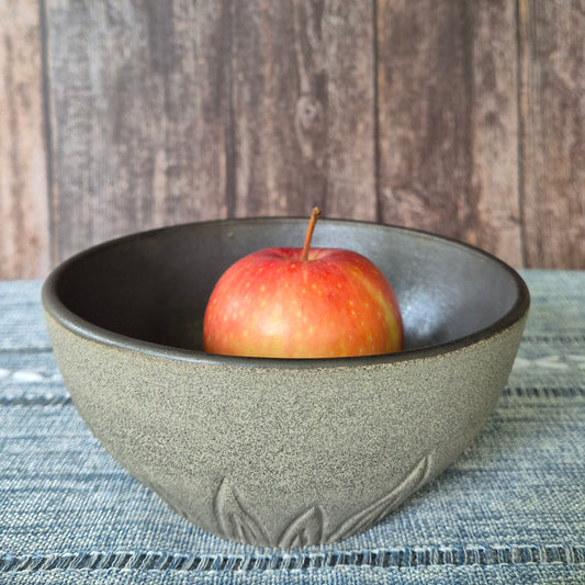 Ceramic bowl with a single apple on a textured surface and wooden background