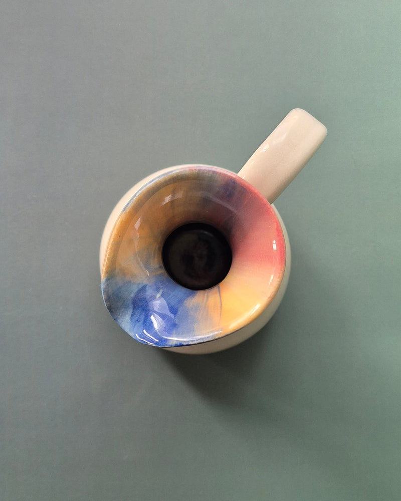 Small ceramic jug with a multicolored design on a gray background