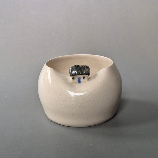 Small cream coloured bud vase featuring a sculptured tiny cottage on the rim. On a grey background