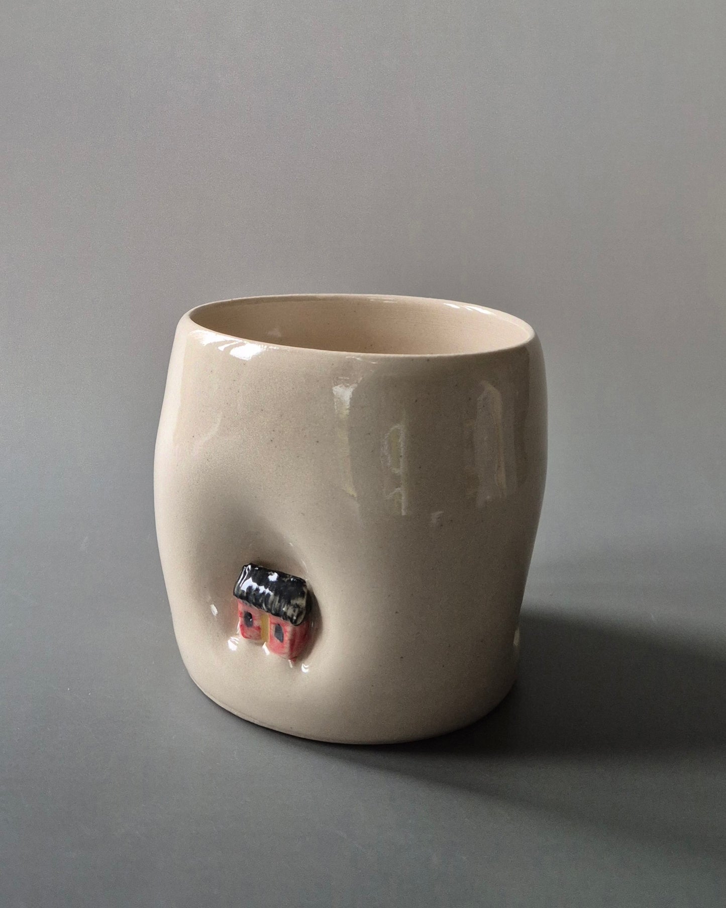 Small white stoneware pot indented with a tiny red cottage. On a grey background