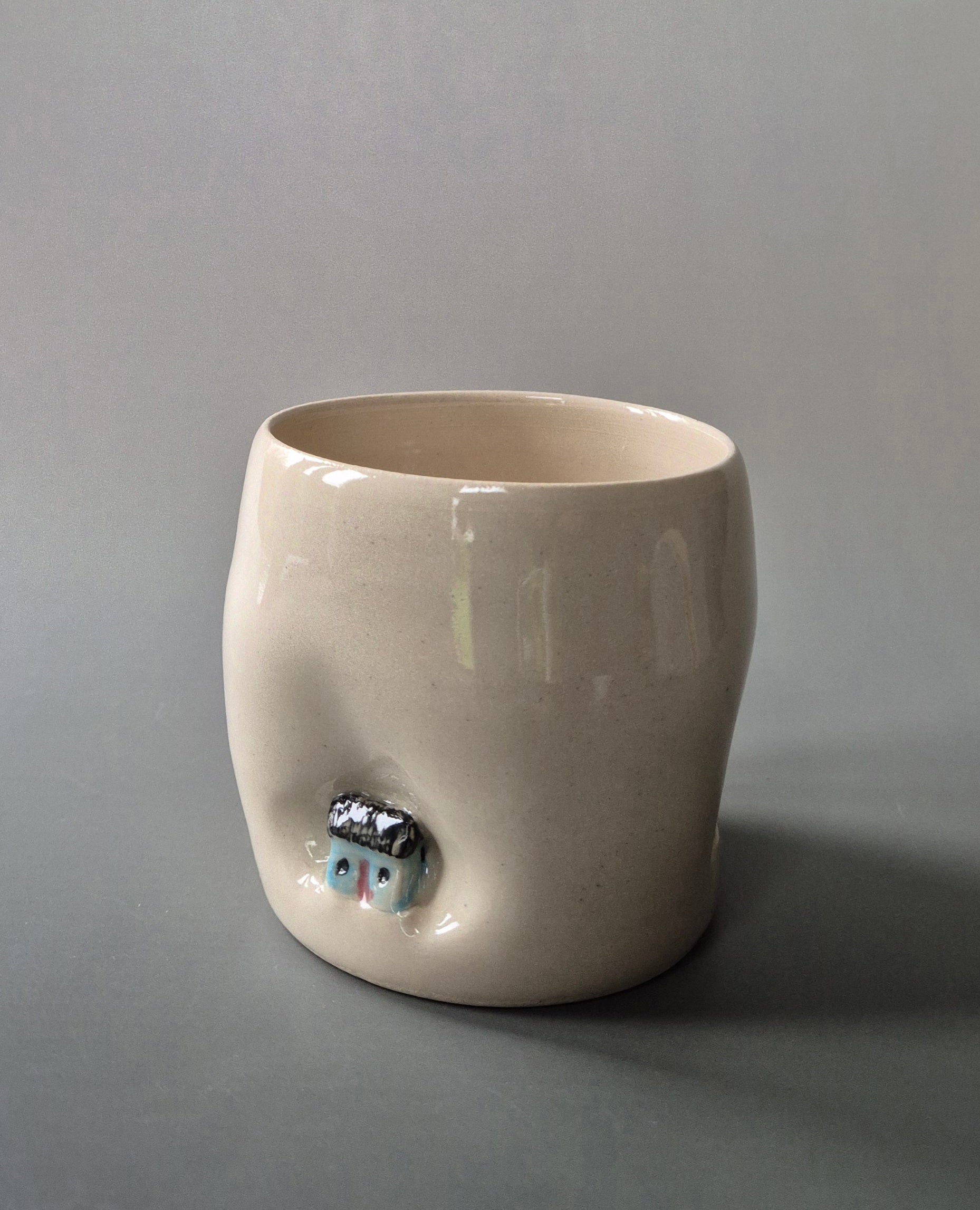 Small white stoneware pot indented with a tiny blue cottage. On a grey background