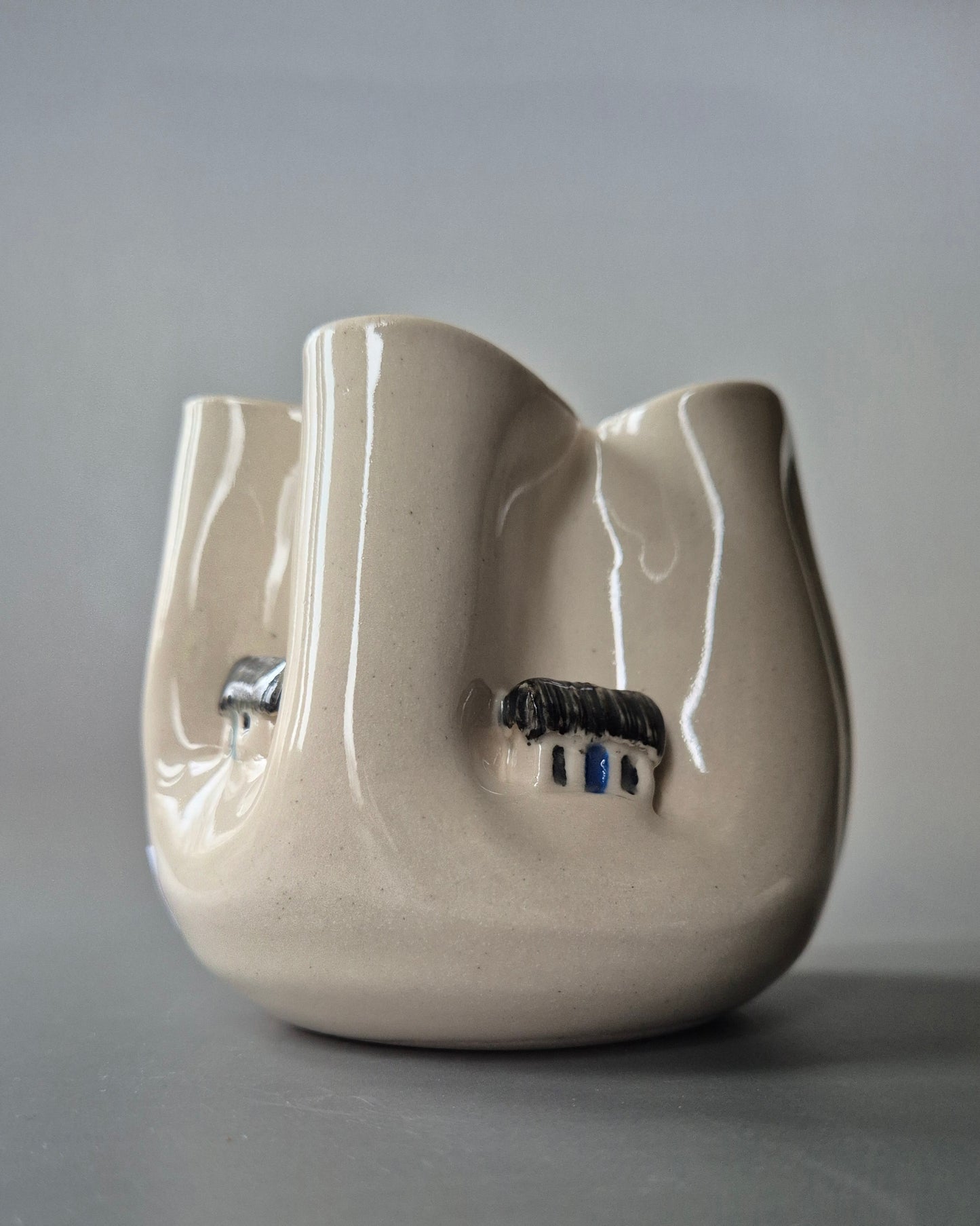 Small white stoneware pot folded to embrace a tiny white cottages. On a grey background