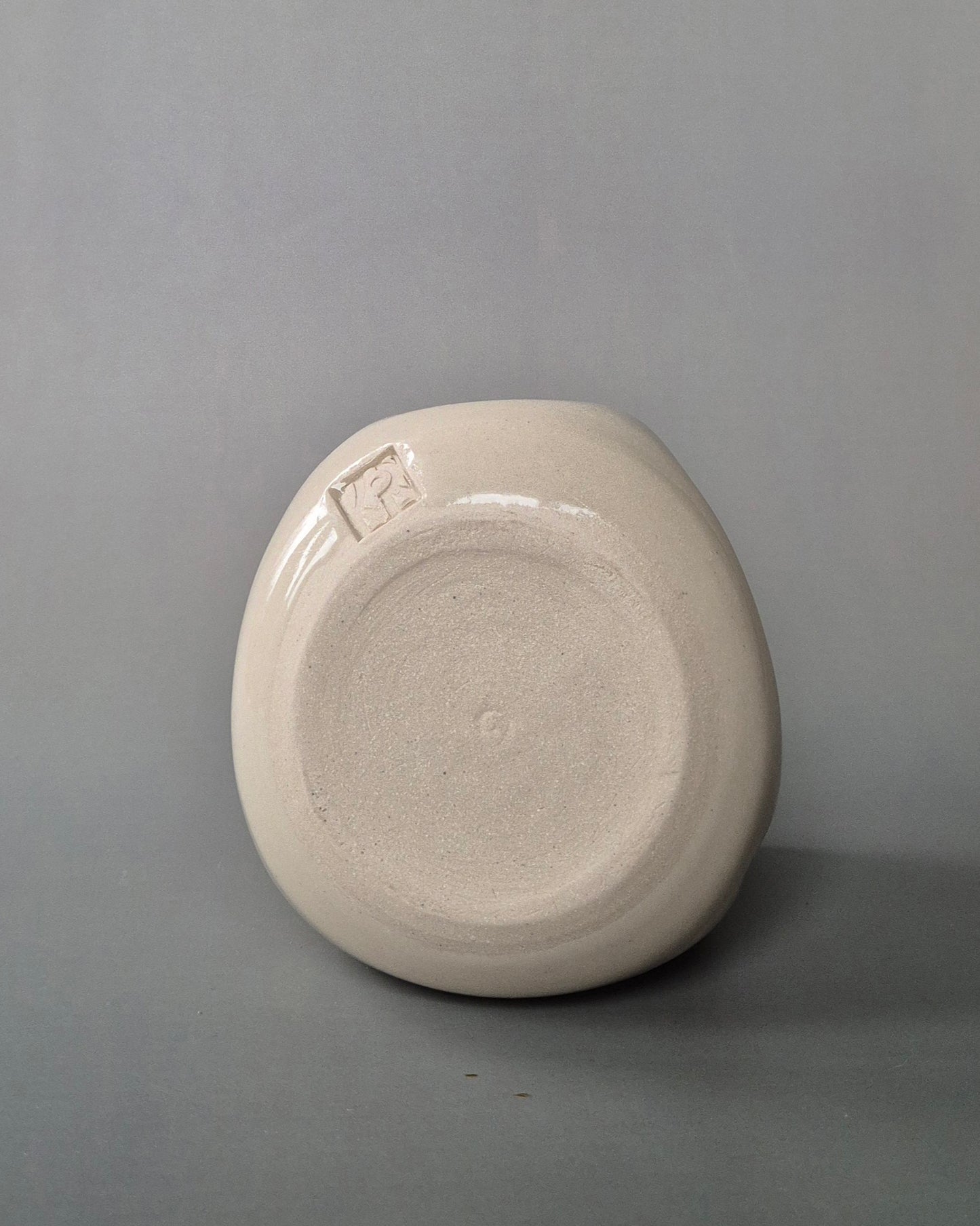 Base of a small white stoneware pot on a grey background