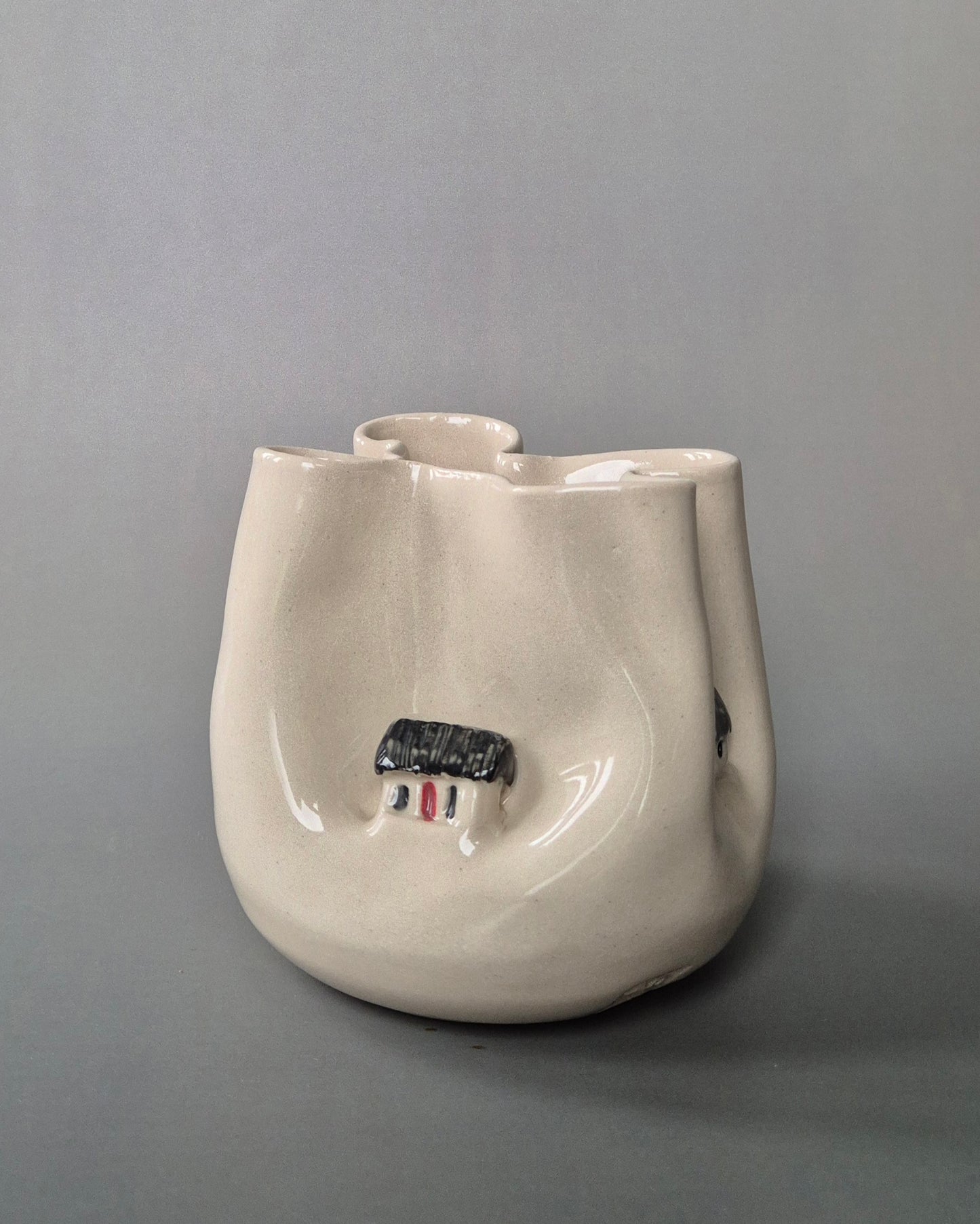 Small white stoneware pot folded to embrace a tiny white cottages. On a grey background
