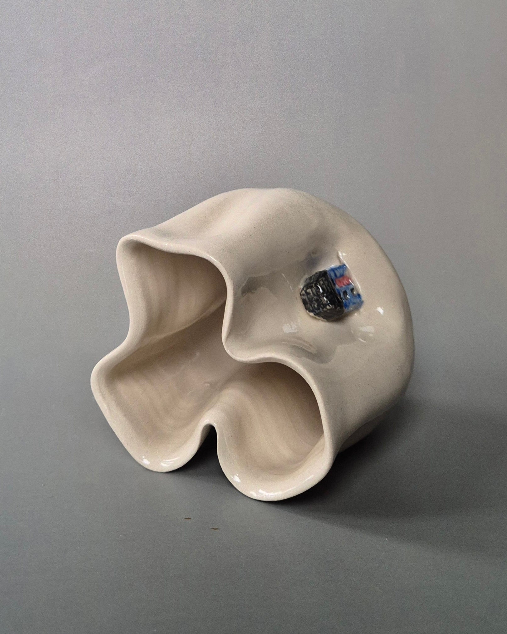 Top view of a small white stoneware pot folded to embrace 3 tiny cottages. On a grey background