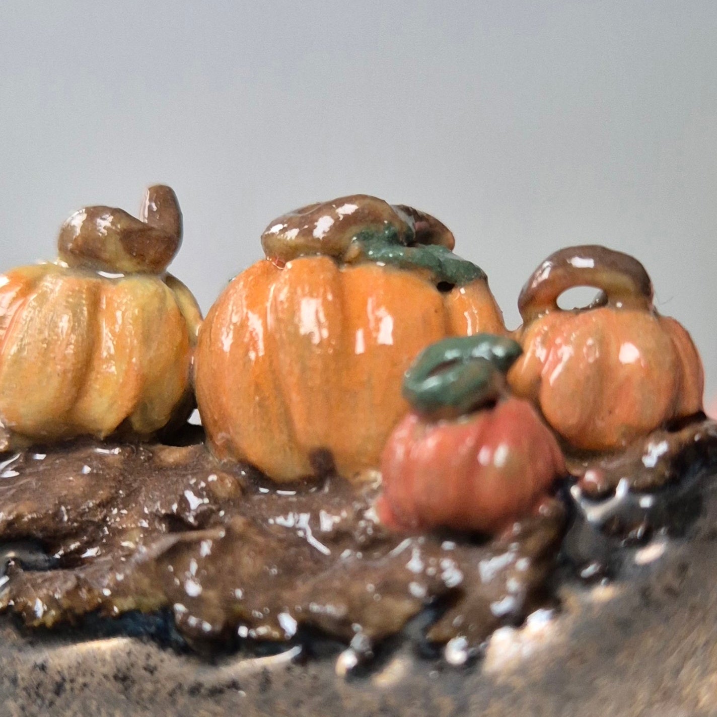 Close-up photo of four tiny ceramic pumpkins on the edge of the bowl with a neutral background.