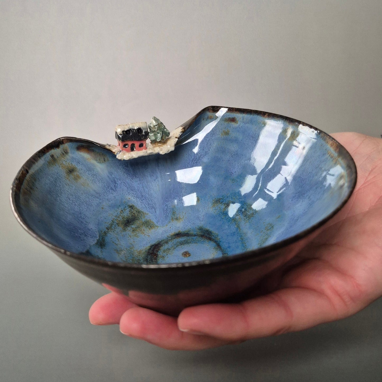 Hand holding a blue ceramic bowl with a small landscape inside on a gray background