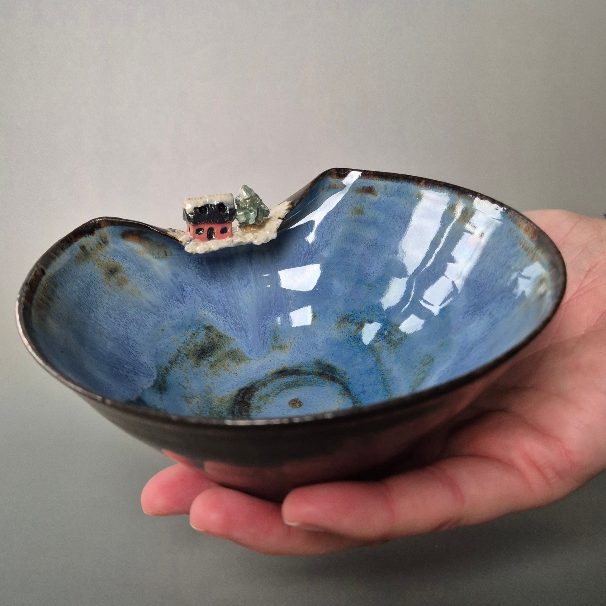 Hand holding a blue ceramic bowl with a small landscape inside on a gray background