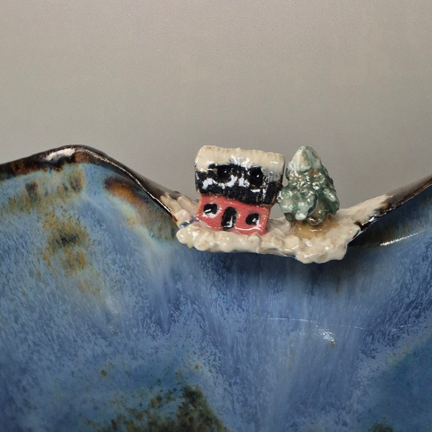 Miniature ceramic house with a tree on a textured blue surface