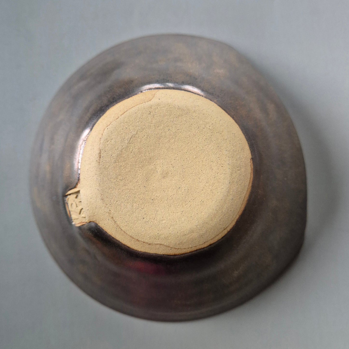 Base of a ceramic bowl with bronze metallic glaze on a grey background.