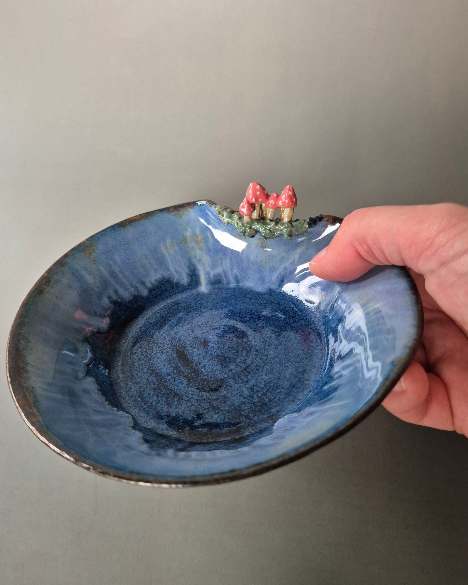 Blue ceramic bowl with decorative elements held by a hand against a neutral background