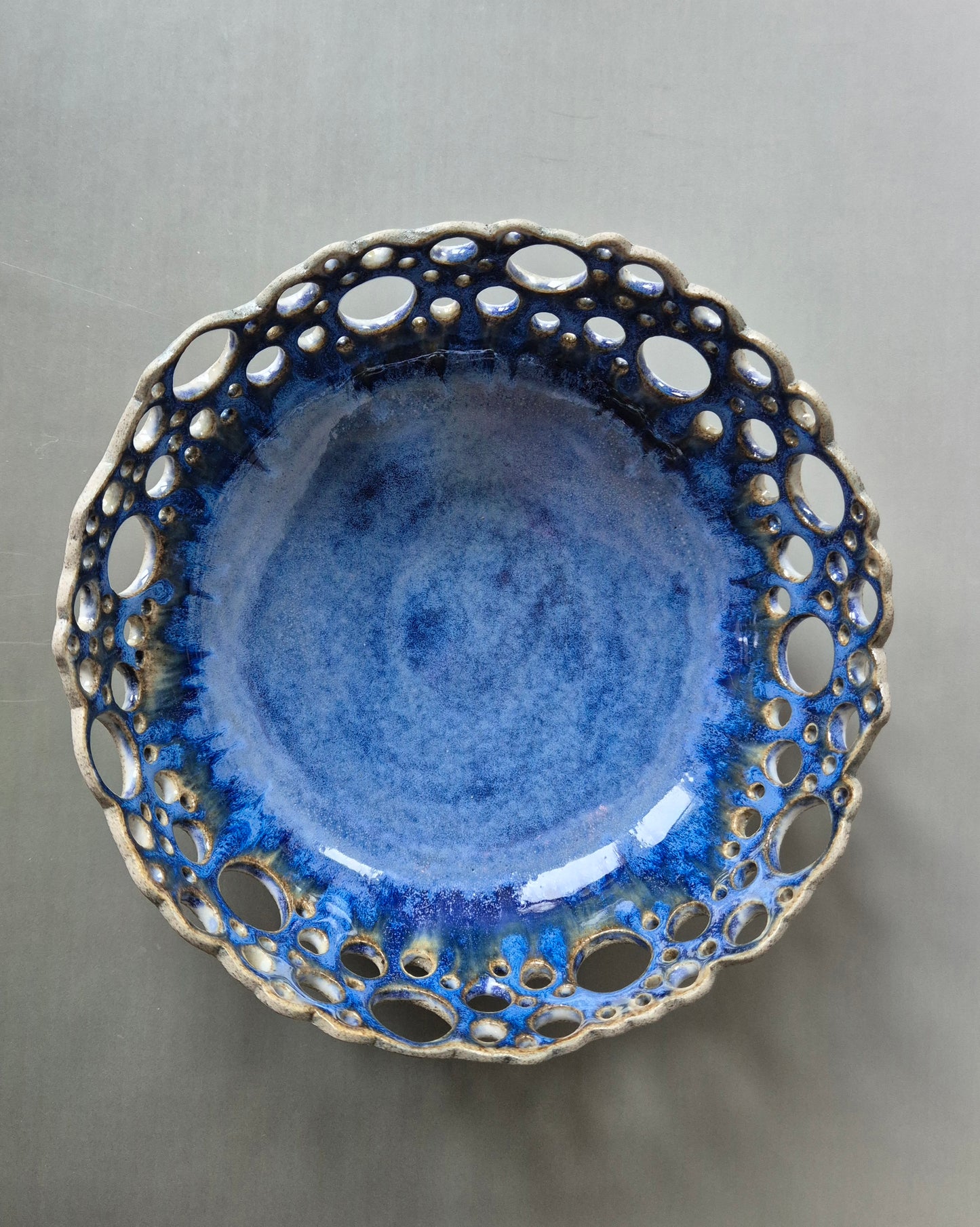 Ceramic bowl with blue glaze and unglazed rim on a gray background