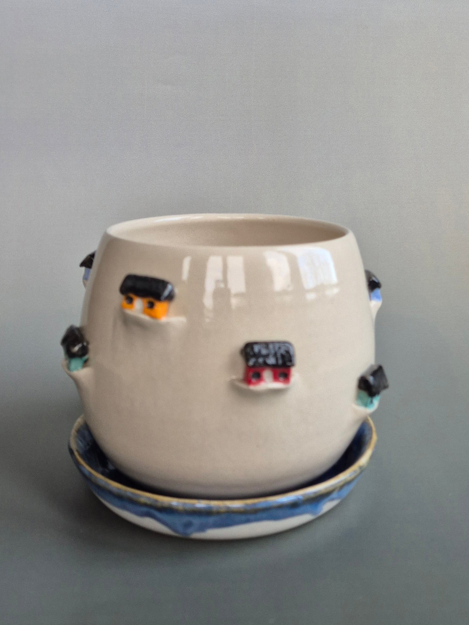 Ceramic planter decorated with colourful tiny houses. On a blue saucer with a plain background