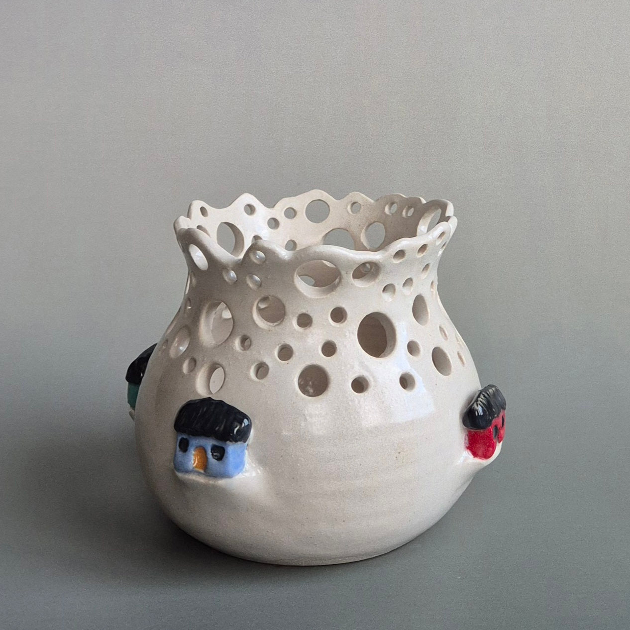Ceramic candle jar with holes and small decorative houses on a gray background