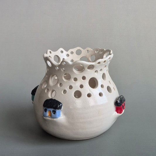 Ceramic candle jar with holes and small decorative houses on a gray background