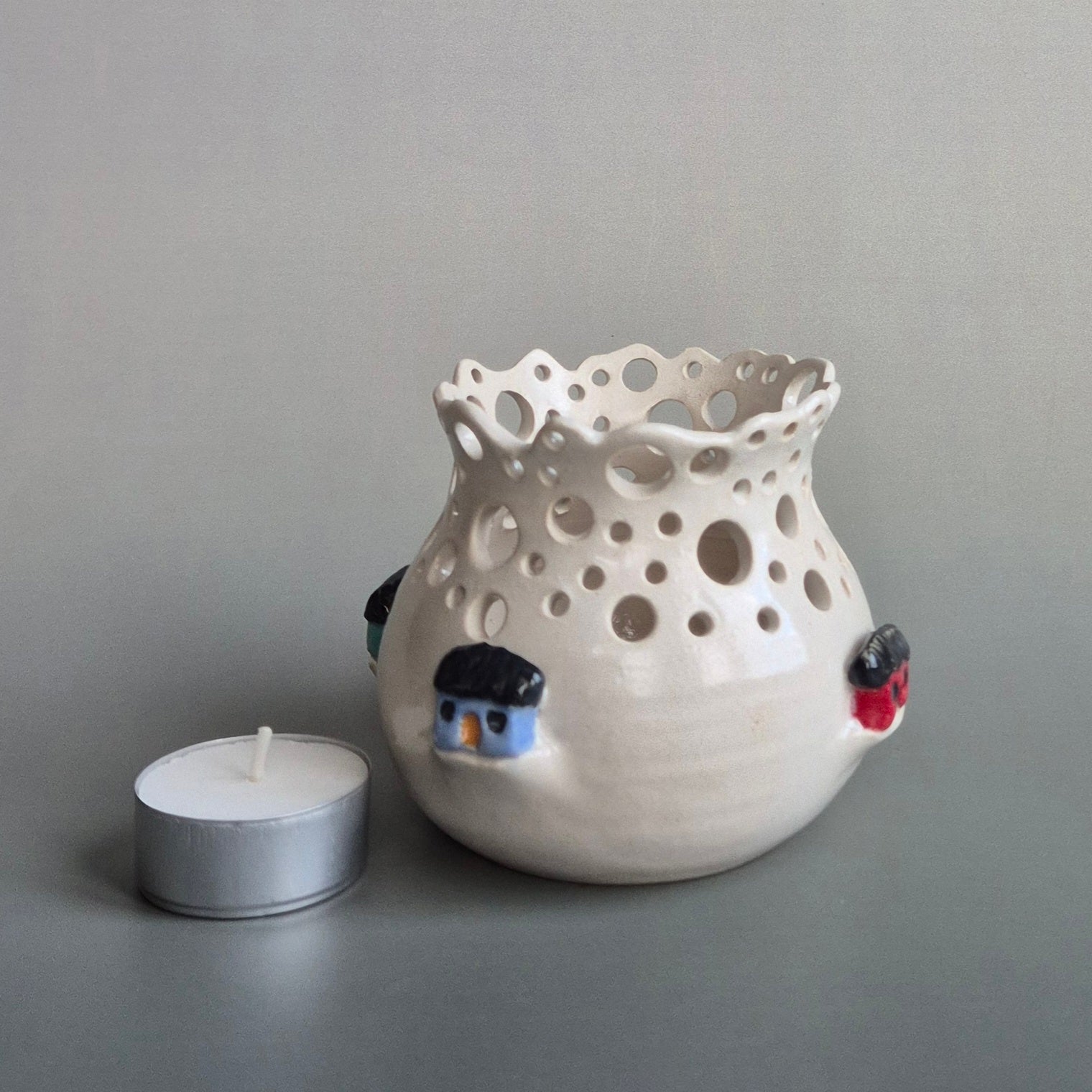 Ceramic candle jar with holes and small decorative houses on a gray background