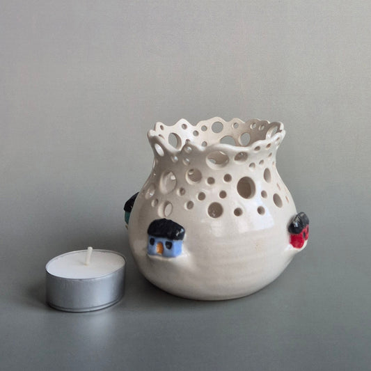 Ceramic candle jar with holes and small decorative houses on a gray background