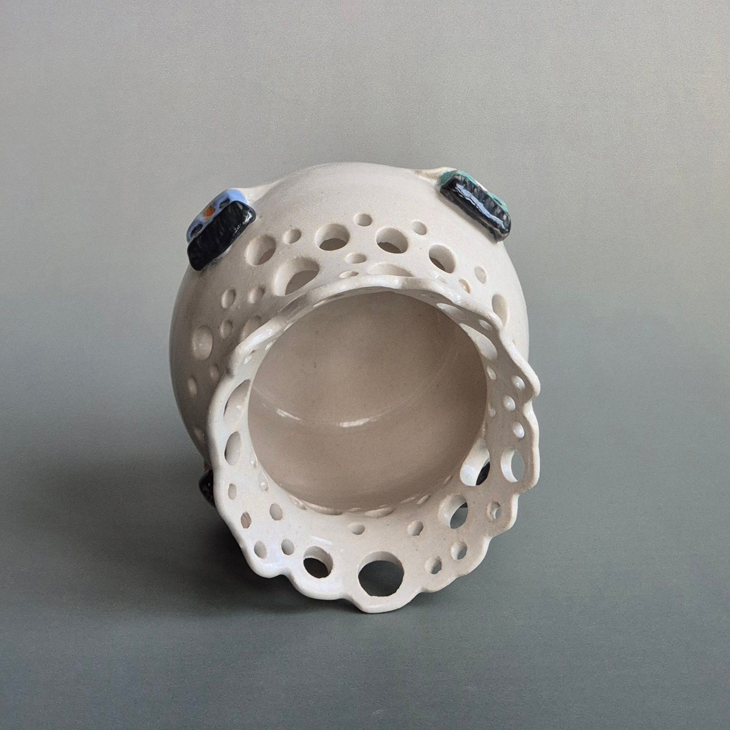 Ceramic candle jar with holes and small decorative houses on a gray background