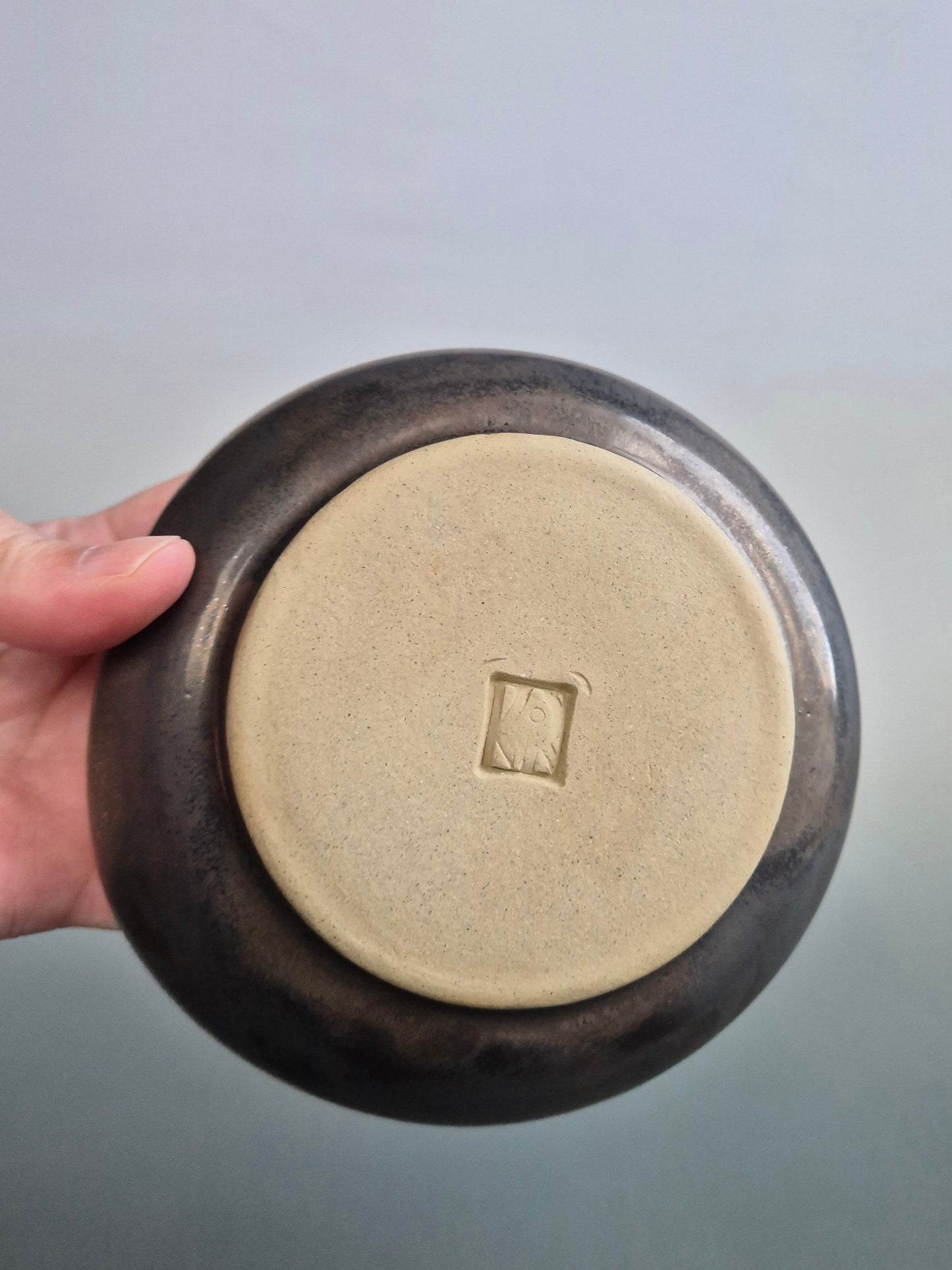 Base of the bronze toadstool bowl, showing the potters mark. On a grey background