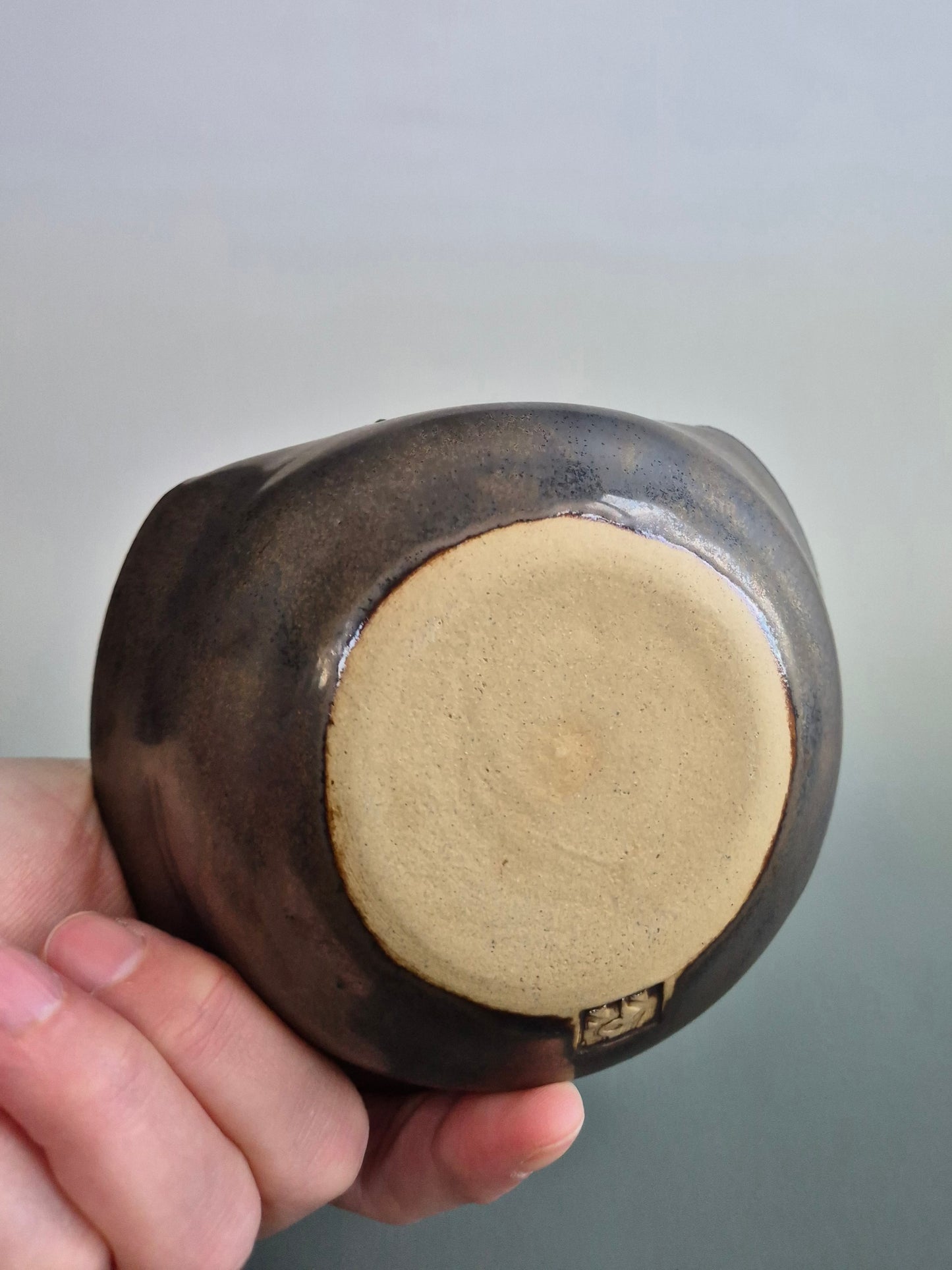 Hand holding a small bronze coloured trinket dish to show the plain base of the dish. On a plain background