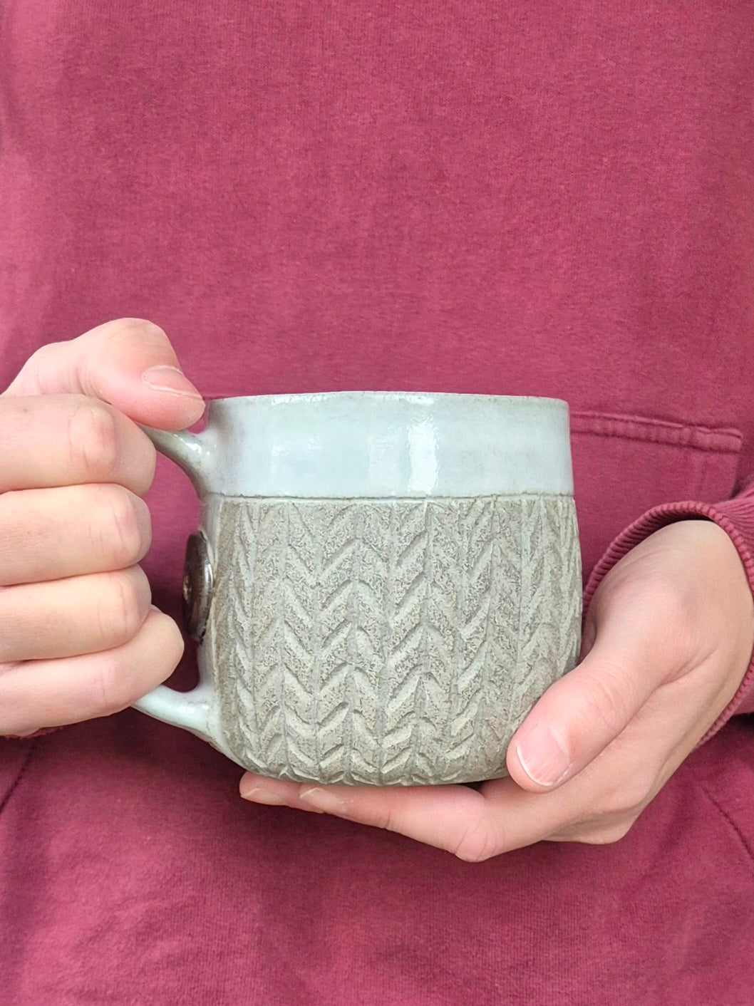 Person holding a textured mug with a maroon sweater background