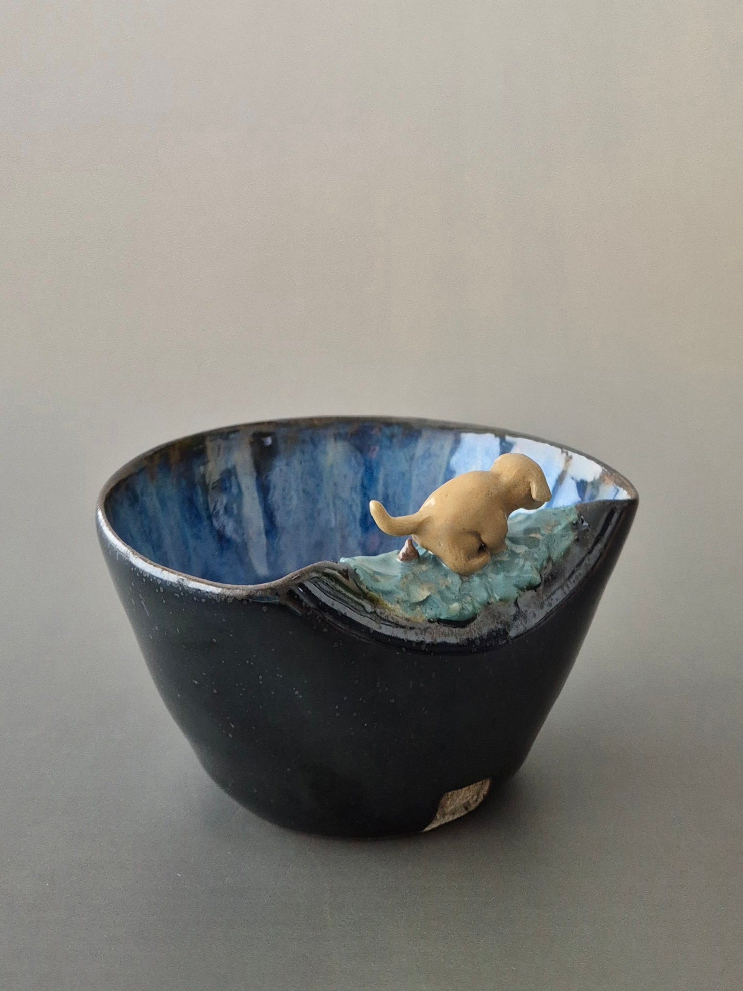 Blue ceramic bowl with a small dog figurine on a plain background