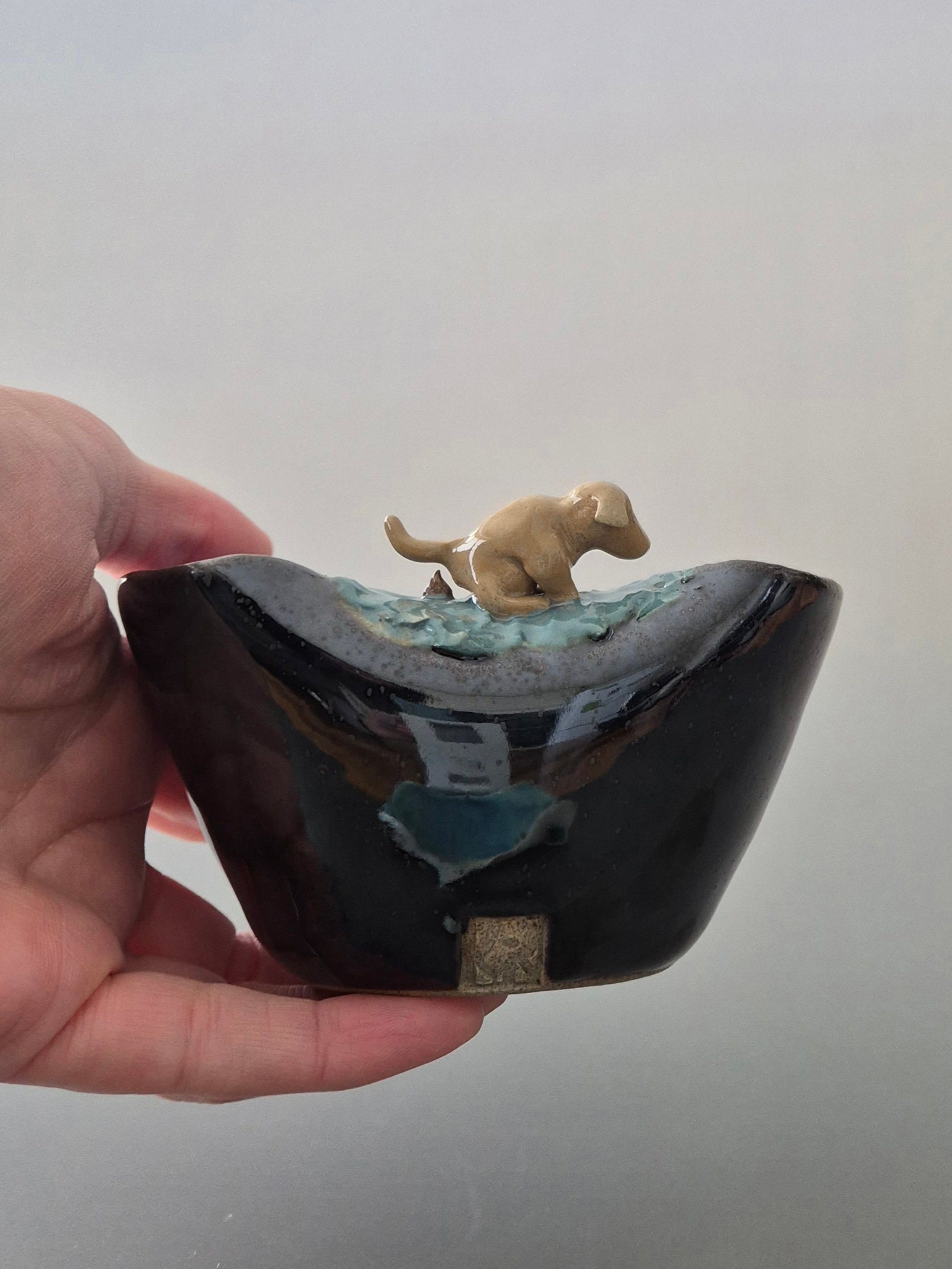Blue ceramic bowl with a small dog figurine on a plain background