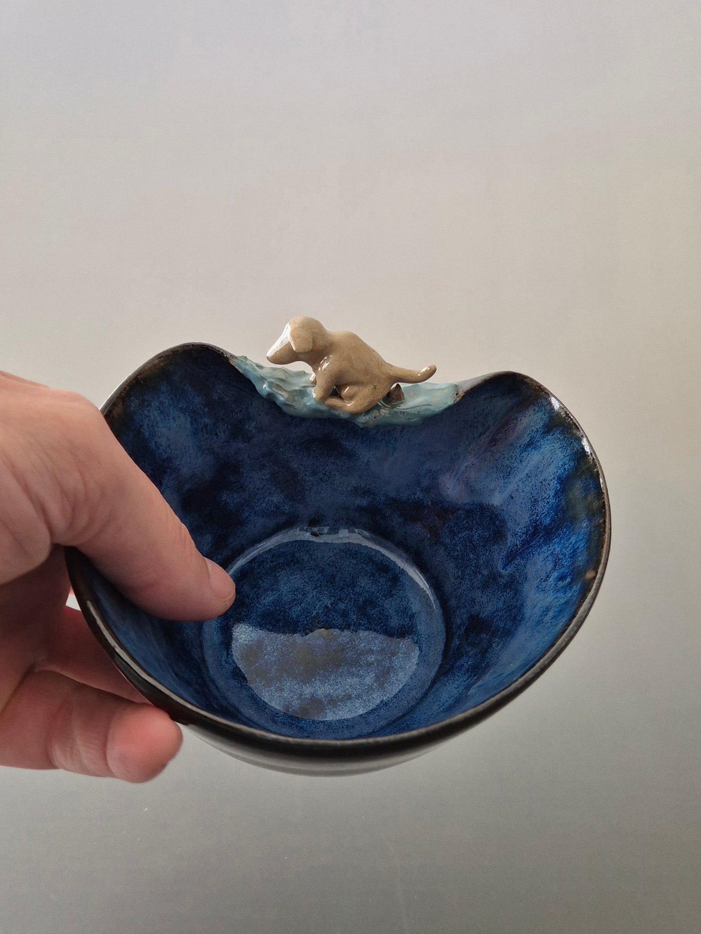 Blue ceramic bowl with a small dog figurine on a plain background