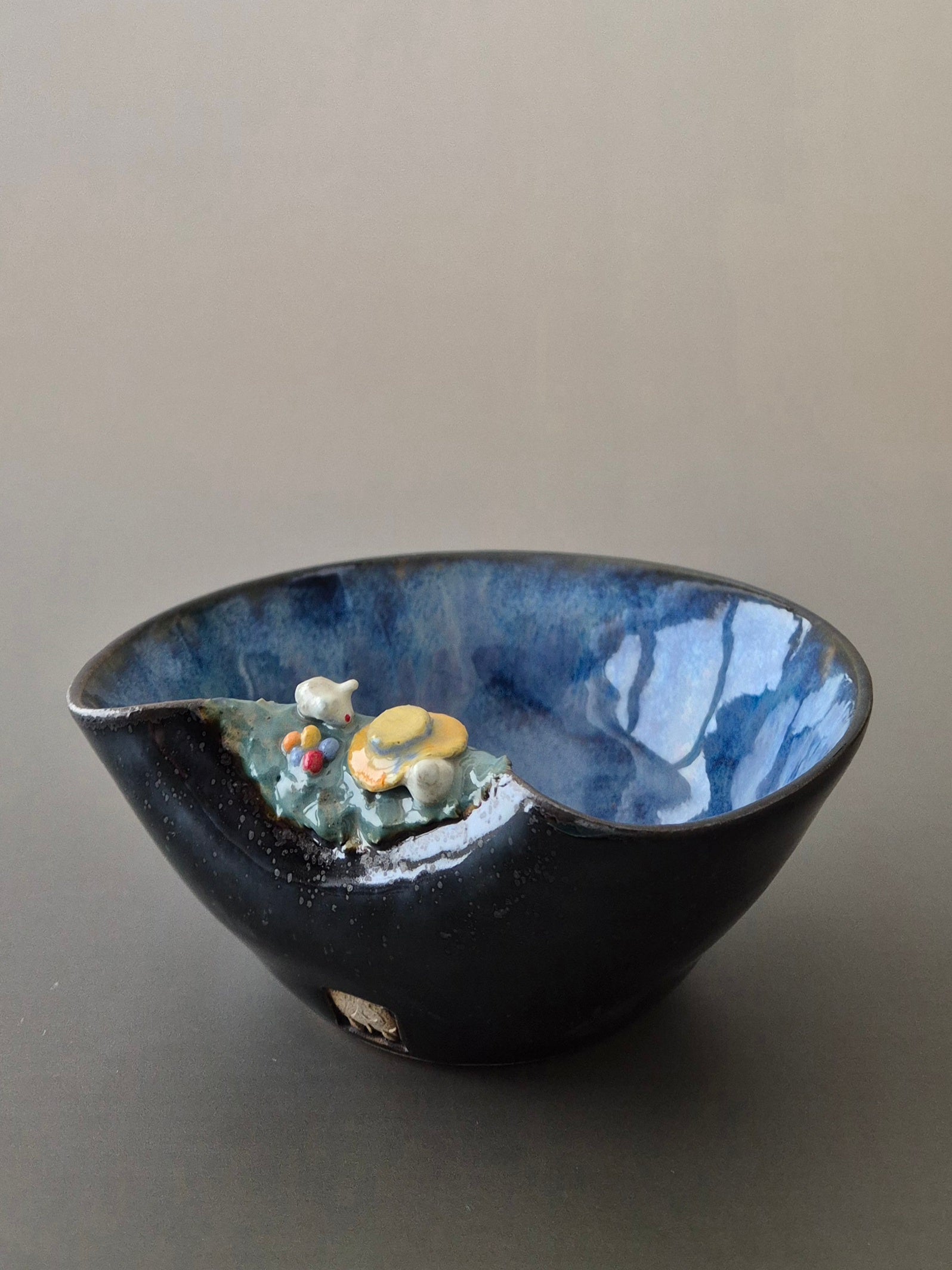 A small ceramic bowl featuring two sculpted easter bunnies playing hide and seek. On a plain background.