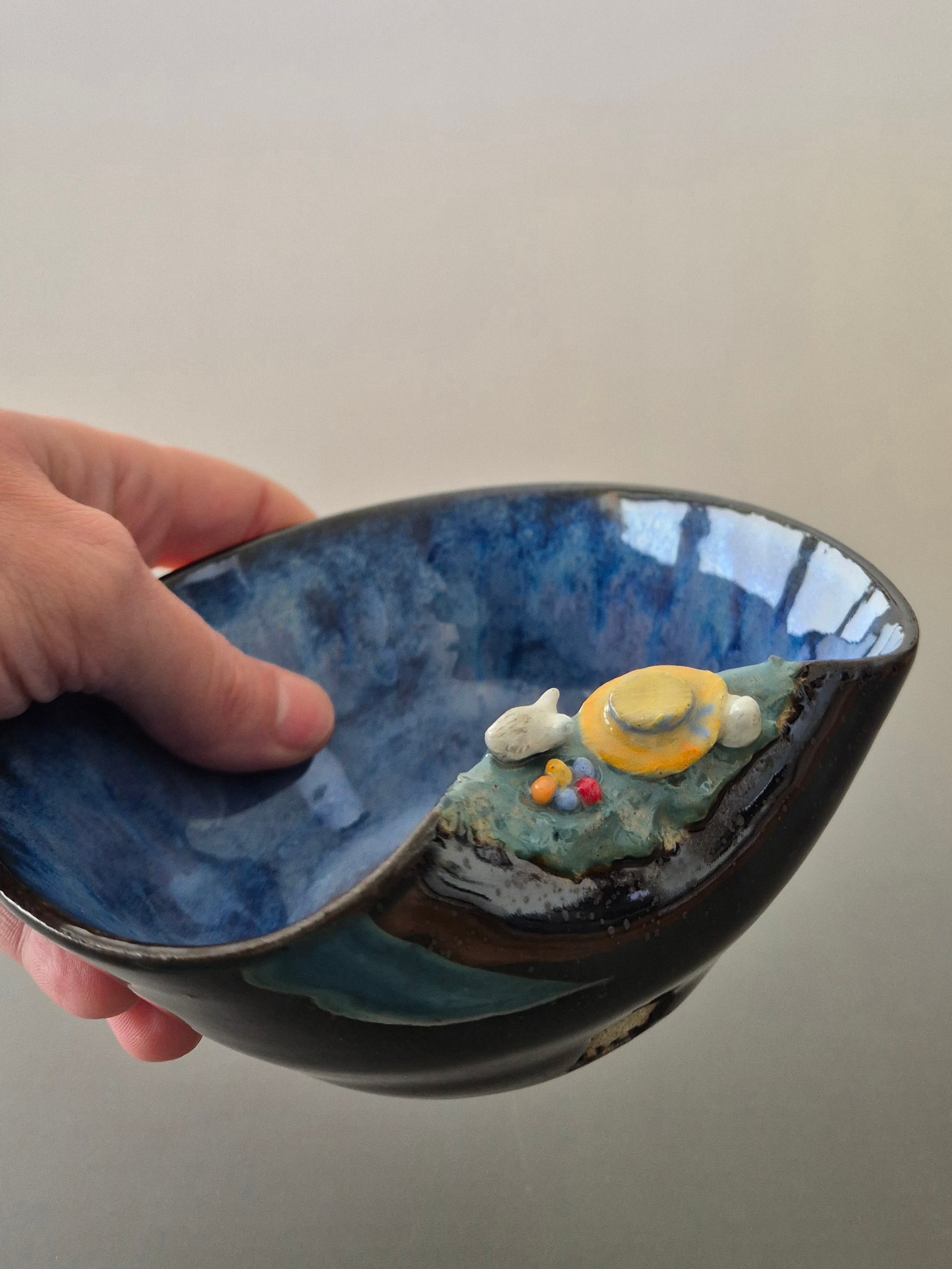 A hand holding a small ceramic bowl featuring two sculpted easter bunnies playing hide and seek. On a plain background.
