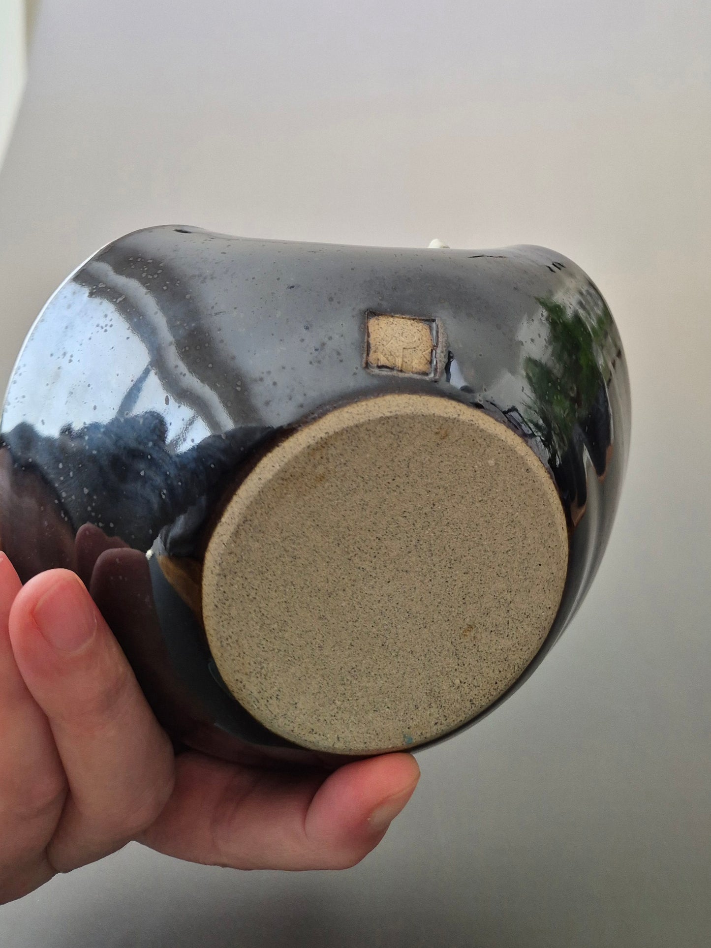 Base of a ceramic bowl being held in a person's hand. On a plain background