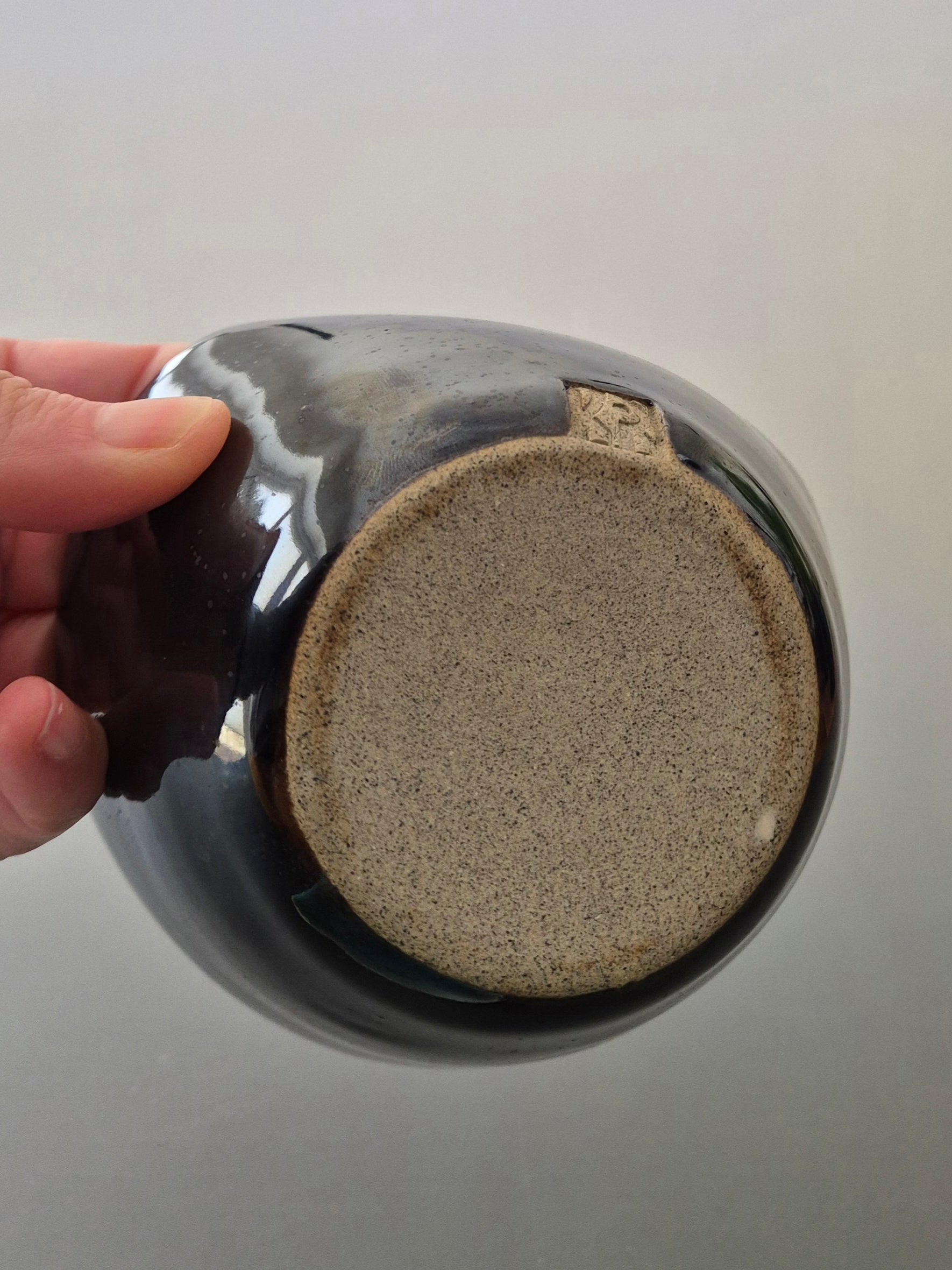 Ceramic mug with textured base held by a hand against a neutral background