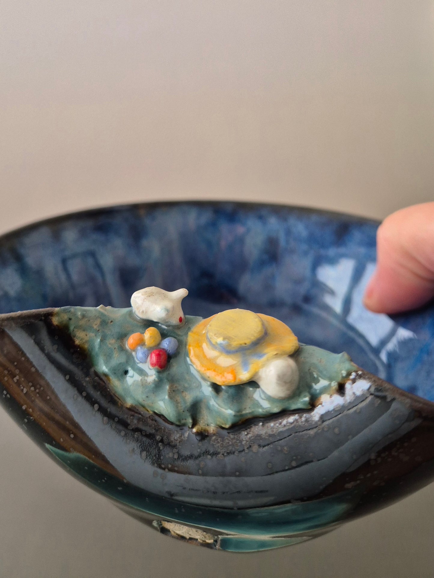 A hand holding a small ceramic bowl featuring two sculpted easter bunnies playing hide and seek. On a plain background.