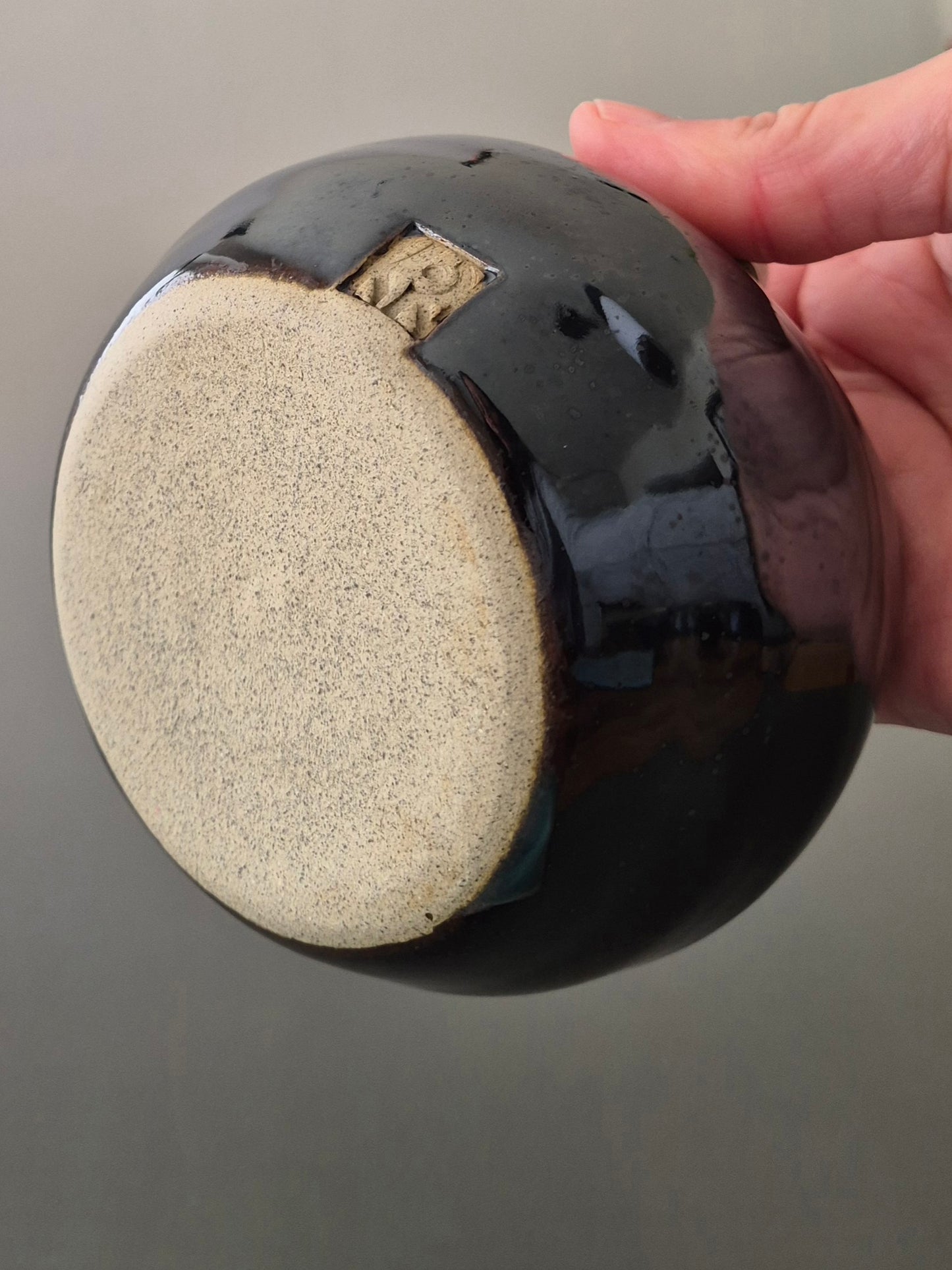 Person holding a bowl to show the base and makers mark against a gray background