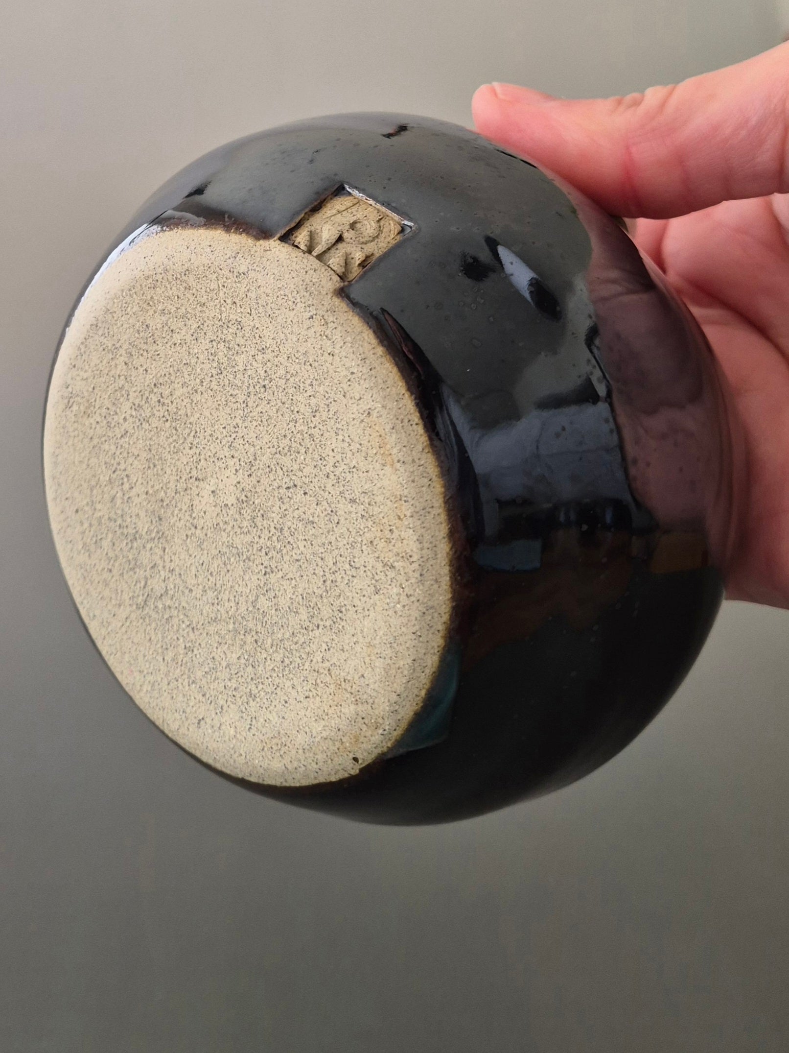 Person holding a bowl to show the base and makers mark against a gray background