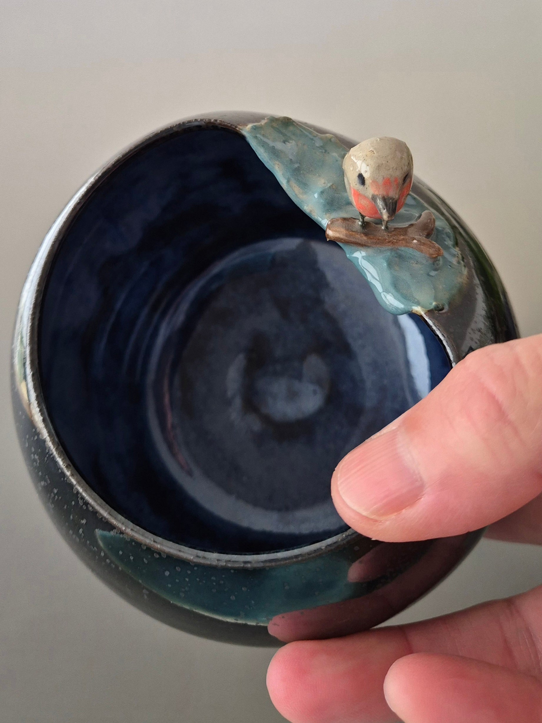 Ceramic bowl with a decorative bird on a branch, held by a hand against a neutral background