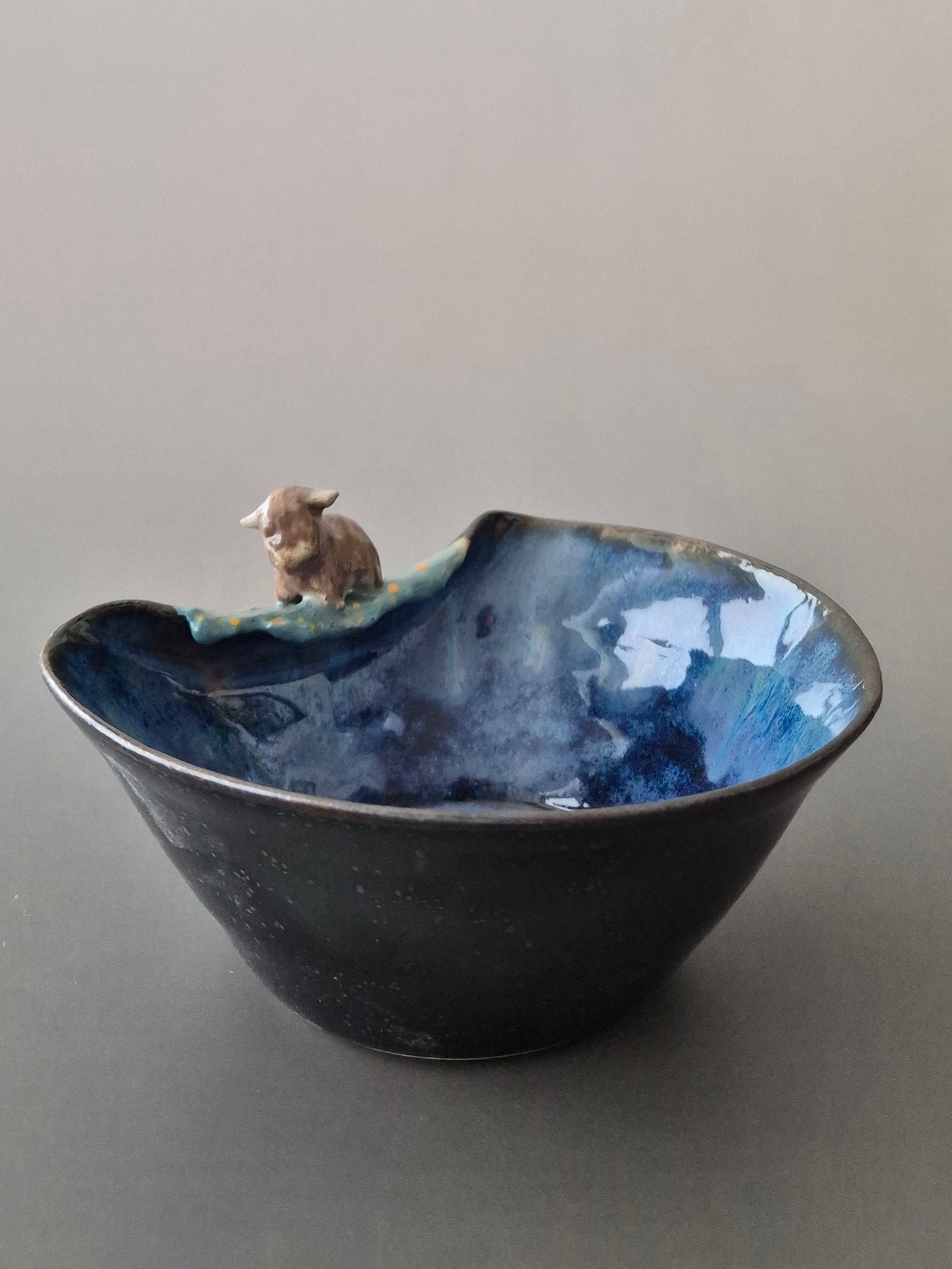 Small ceramic bowl with a tiny sculpted highland cow. On a grey background