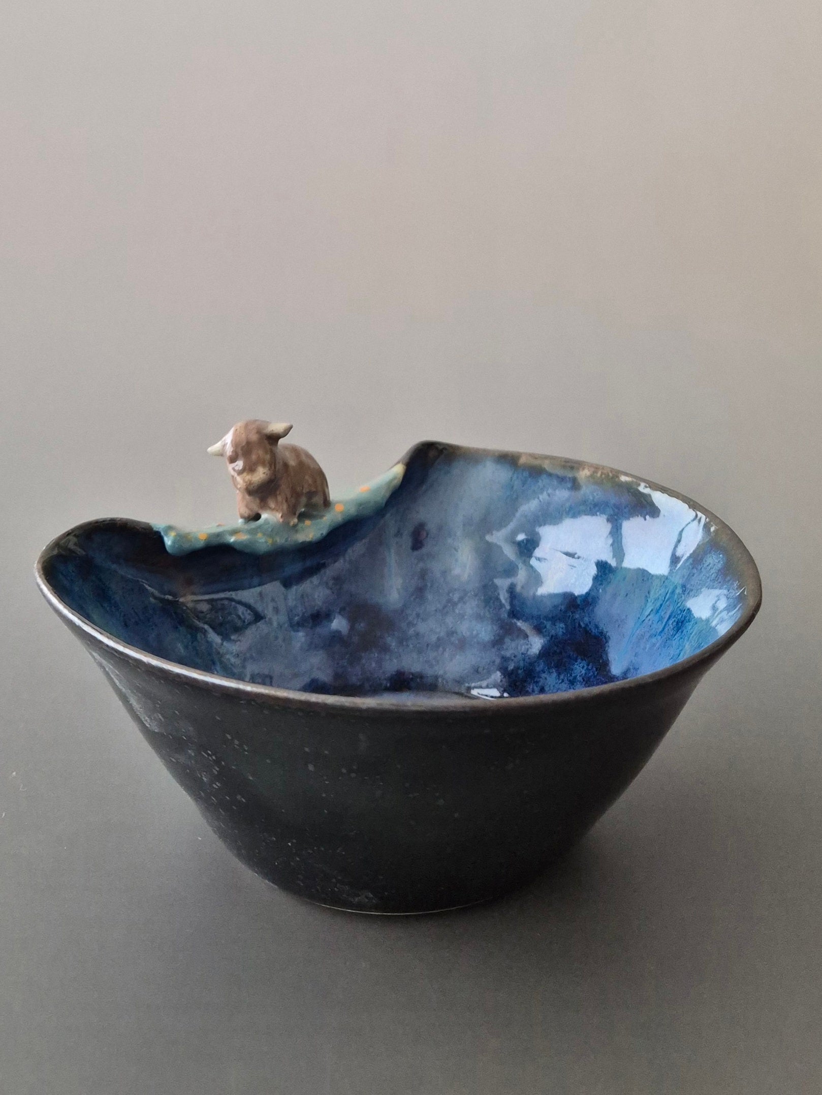 Small ceramic bowl with a tiny sculpted highland cow. On a grey background