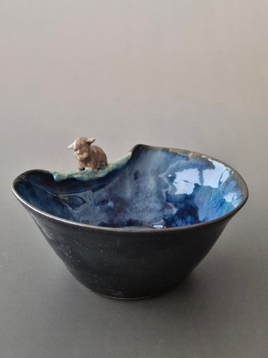 Small ceramic bowl with a tiny sculpted highland cow. On a grey background