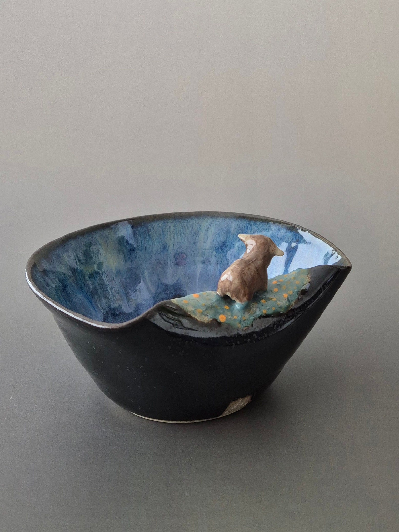 A small ceramic bowl with a tiny sculpted highland cow. On a grey background