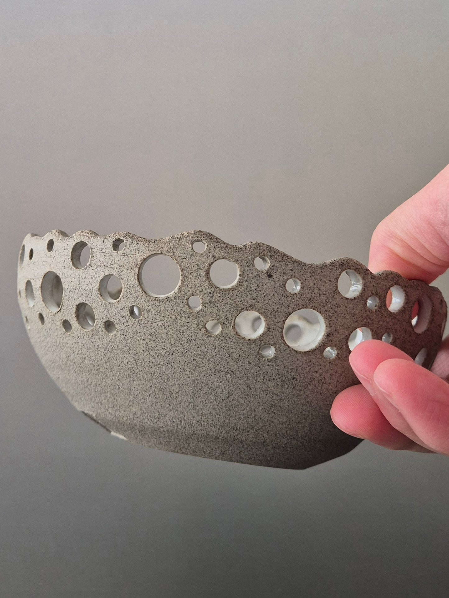 Hand holding a textured ceramic bowl with bubble design against a gray background