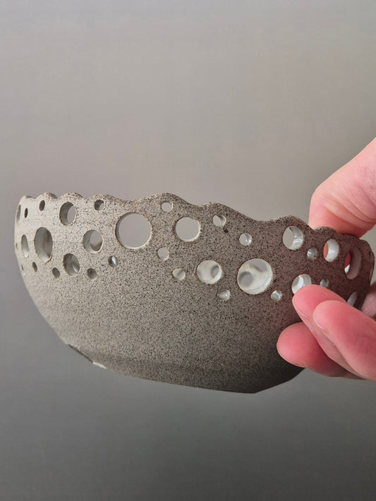 Hand holding a textured ceramic bowl with bubble design against a gray background
