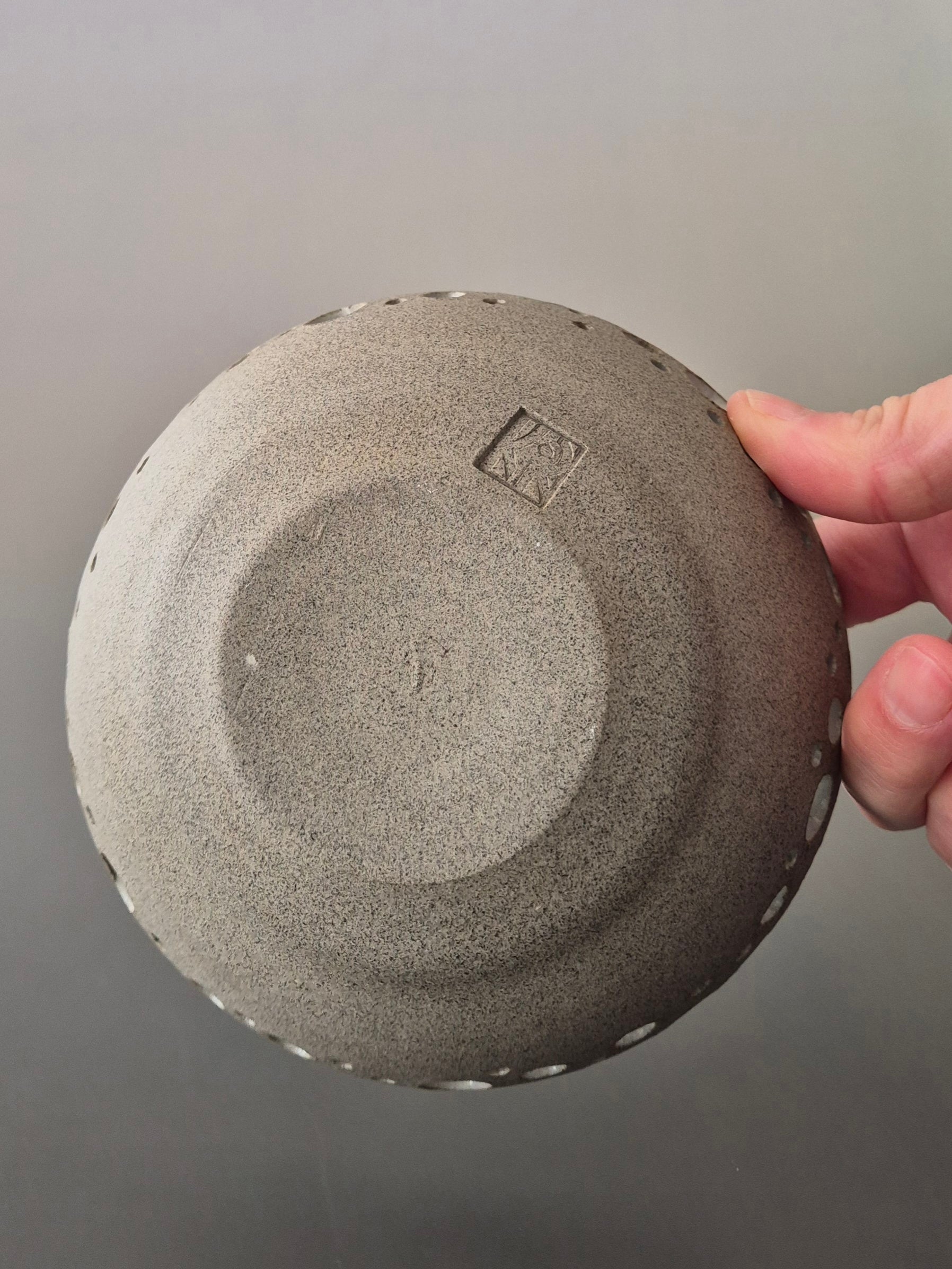 Person holding a textured gray dish to show the base against a neutral background