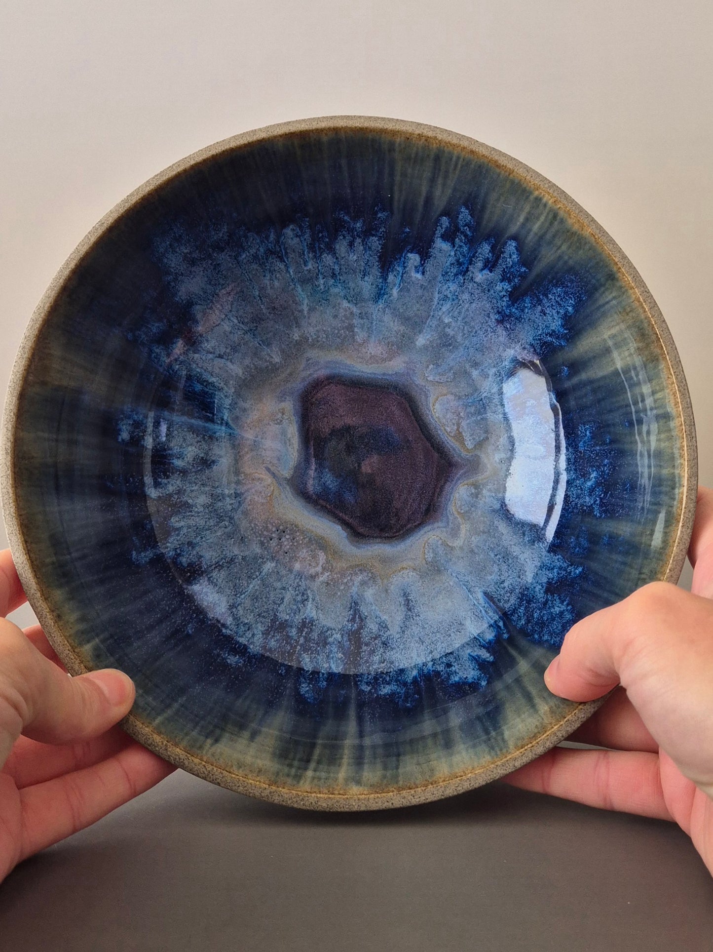 Ceramic bowl with blue and white glaze held by two hands against a neutral background