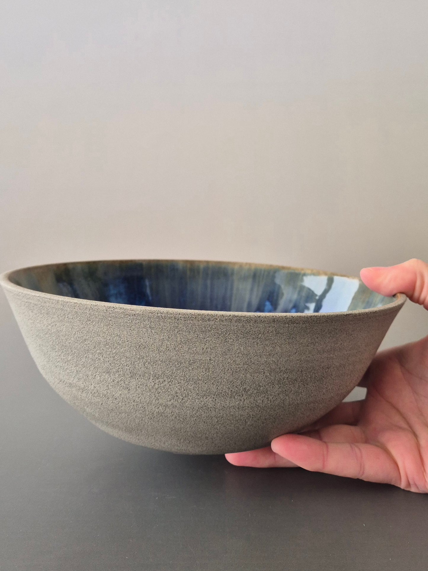 Hand holding a textured ceramic bowl with a blue interior against a neutral background